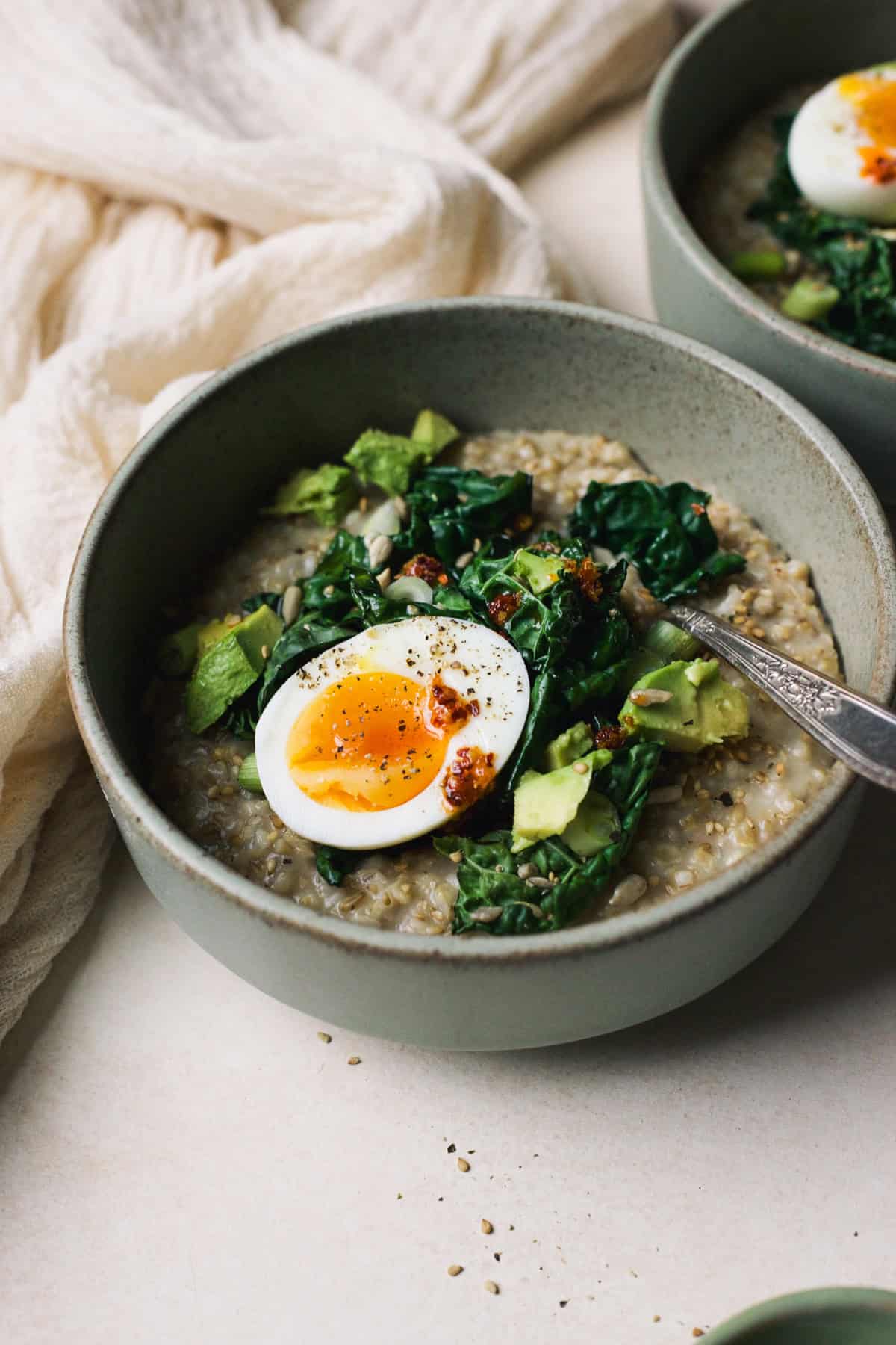 Savory oatmeal in a bowl topped with sautéed kale, jammy egg, and chili crisp.