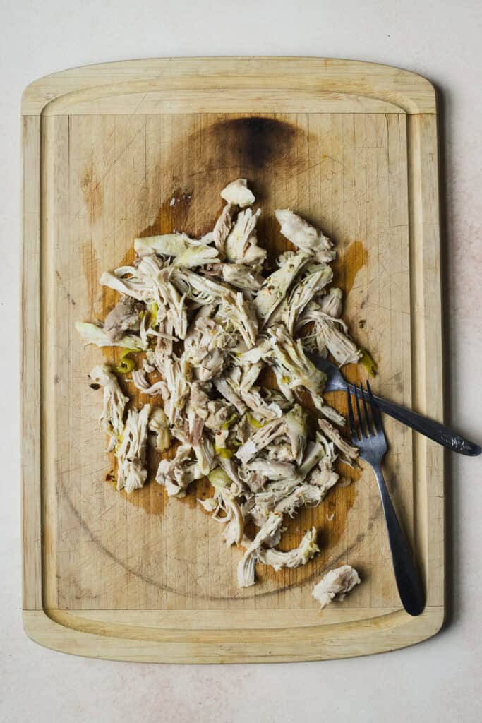 Chicken thighs shredded on bamboo cutting board with two forks.