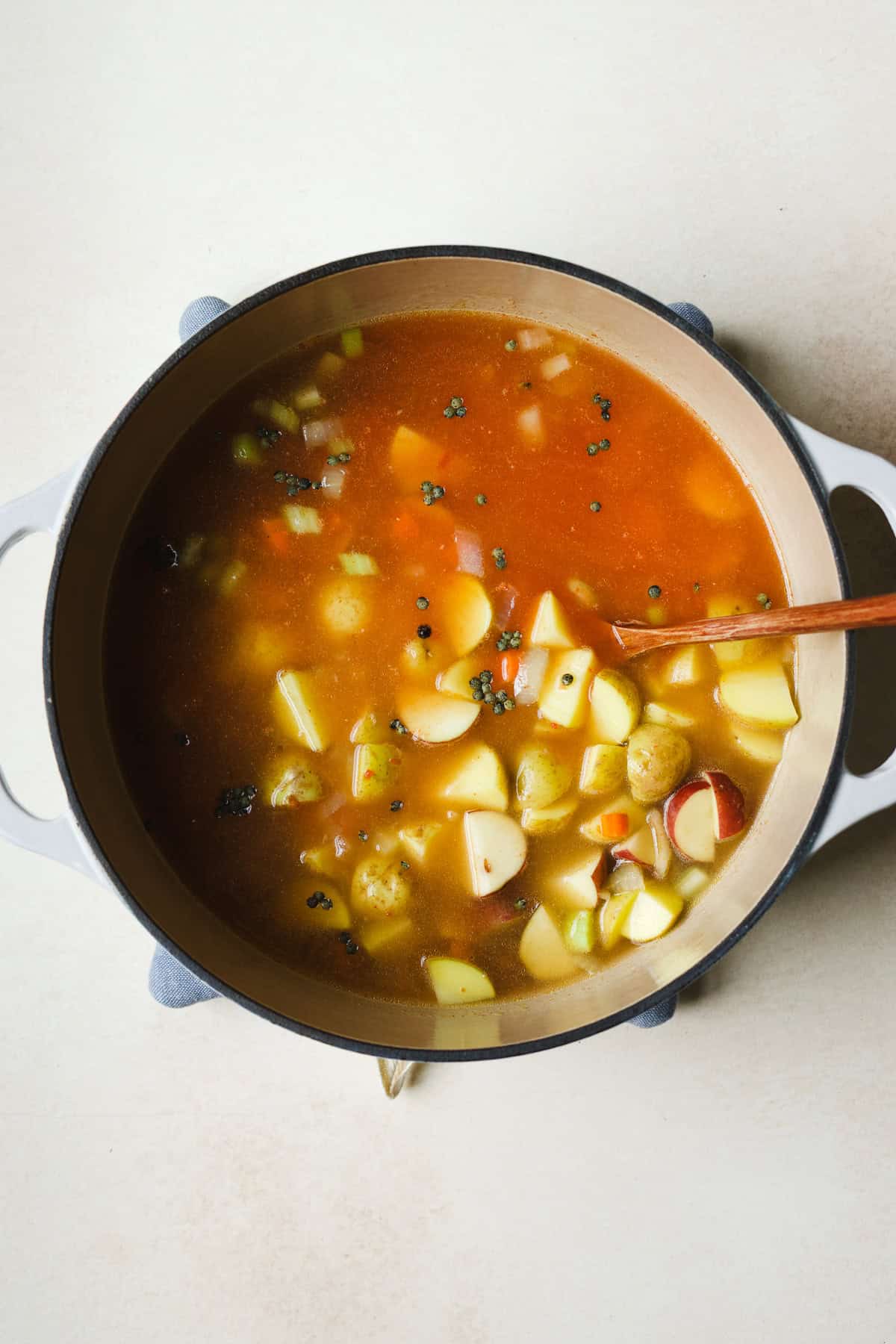 Adding crushed tomatoes, lentils, potatoes, and broth to soup pot.
