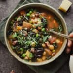 Bowl of spring minestrone with hand scooping a spoonful.