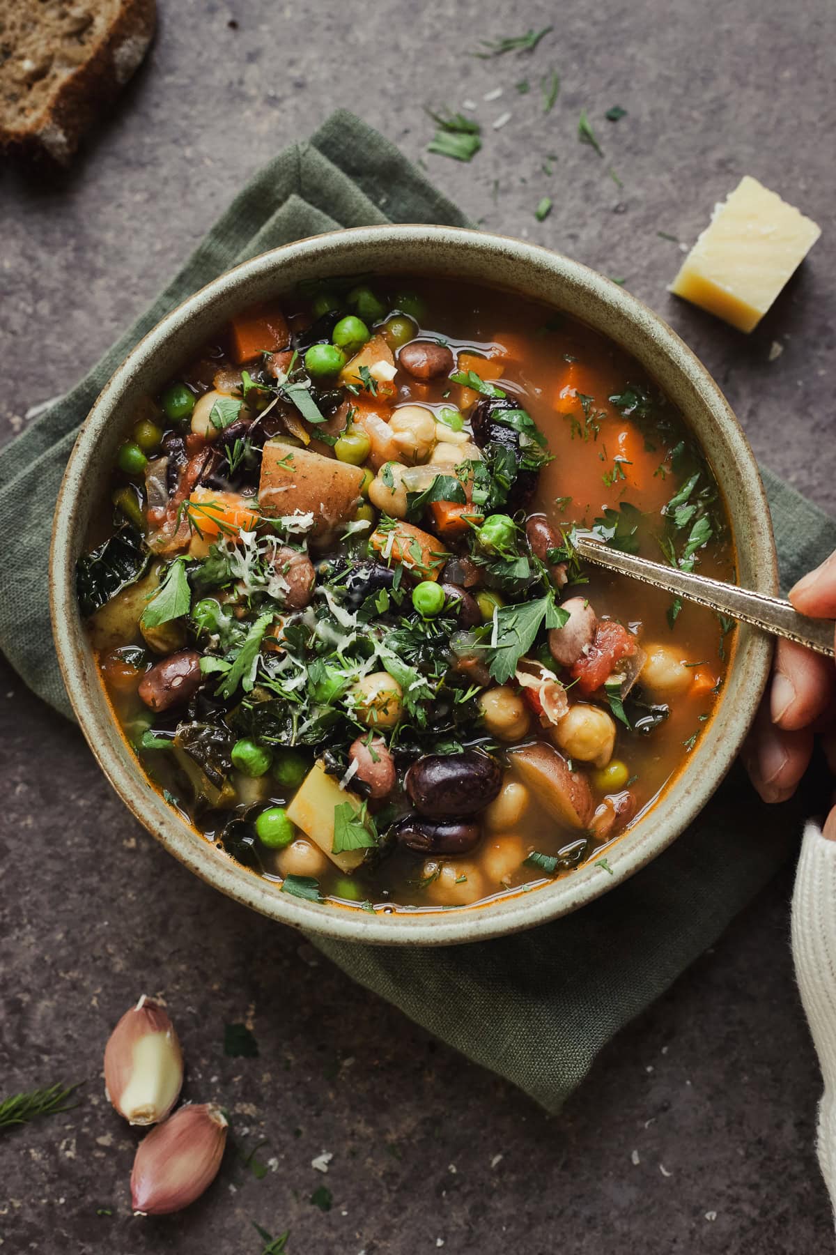 Bowl of spring minestrone with hand scooping a spoonful.