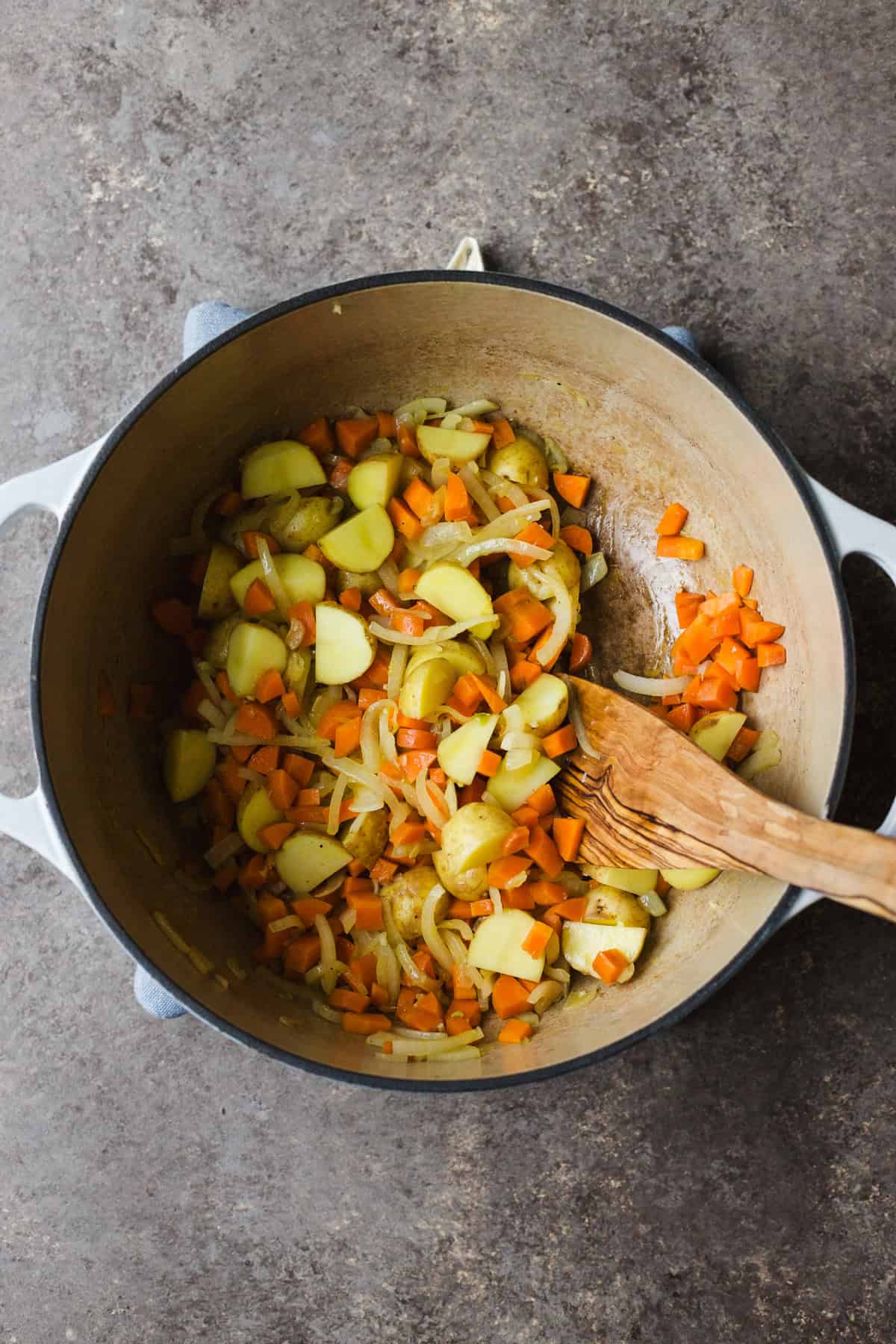Adding potatoes to soup pot with aromatics.