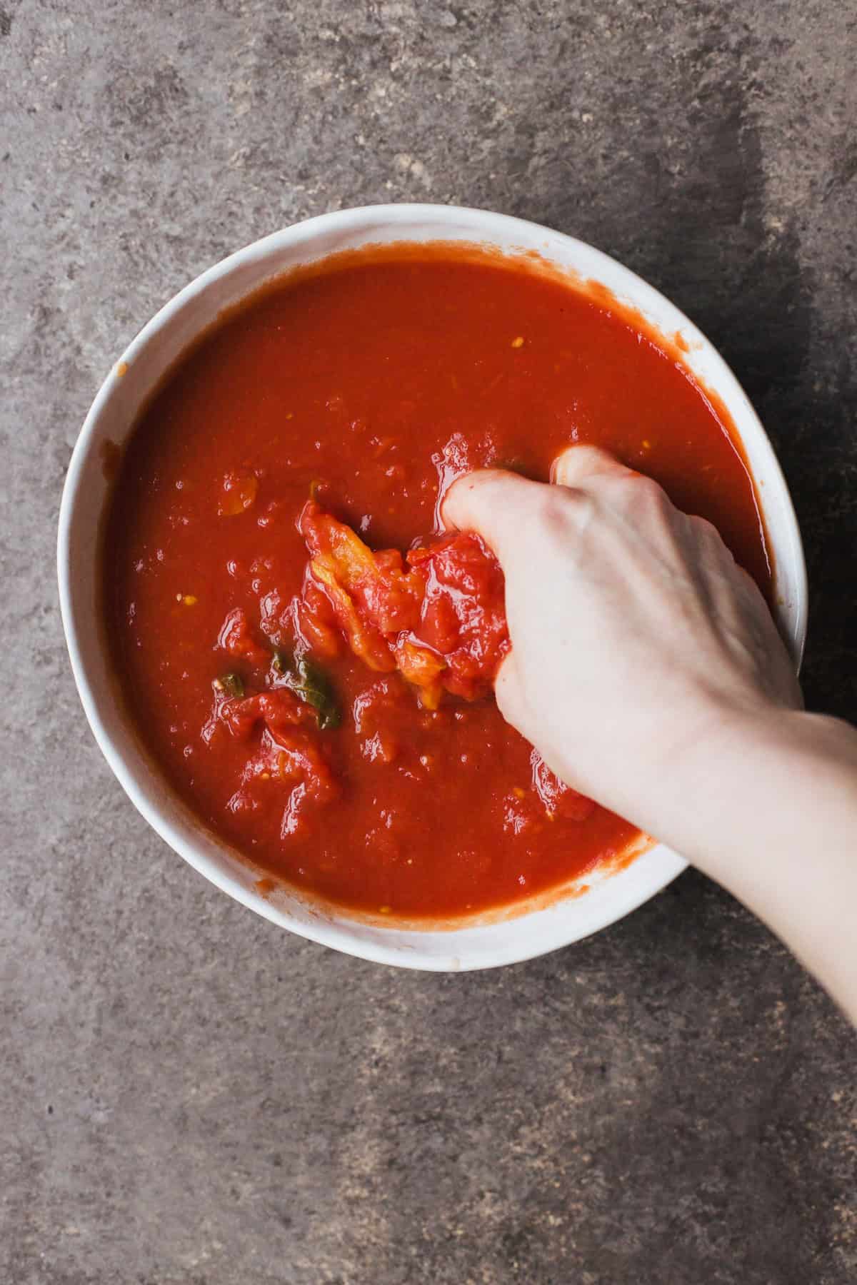 Crushing whole peeled tomatoes with clean hands.