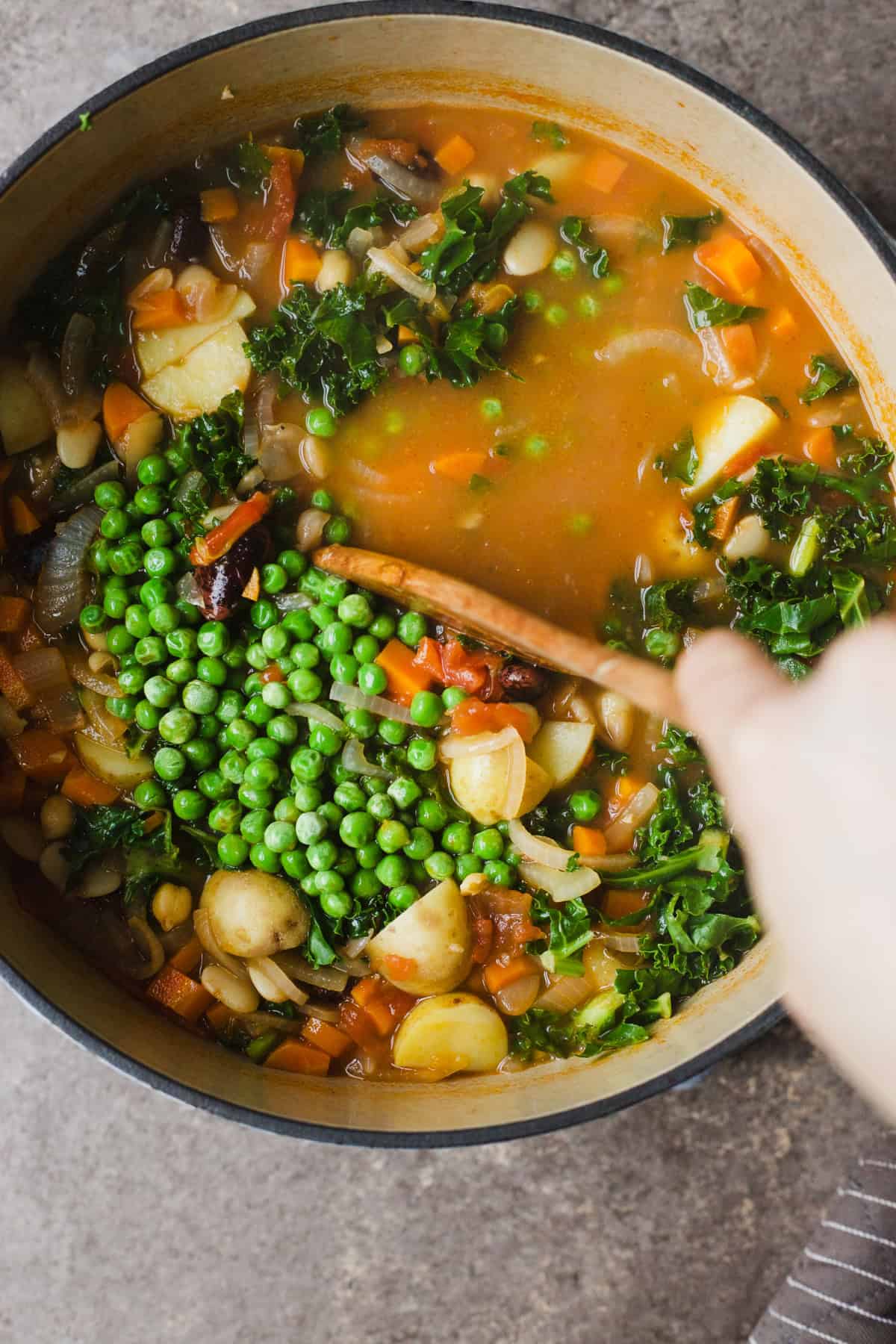 Stirring peas and greens into a large pot of minestrone soup.
