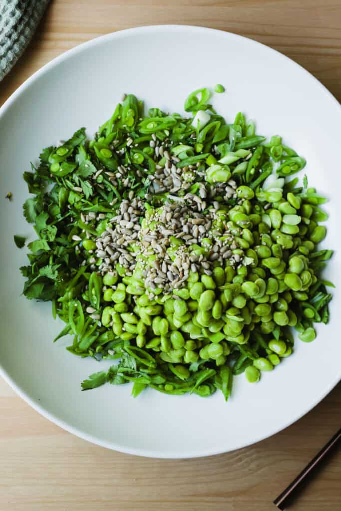Snap pea and edamame salad ingredients combined in a large bowl.