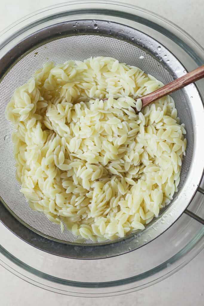 Cooked orzo being drained in a fine mesh sieve.