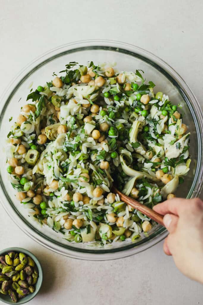 Stirring orzo pasta salad together in a bowl.