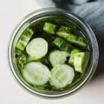 Fridge pickles in a jar with fresh dill, garlic, and black peppercorns.