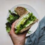 Hand holding tomato and whipped feta sandwich.
