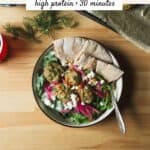 Herby chicken meatball bowls with pita wedges, greens, creamy cucumber salad, feta, and pickled red onions.