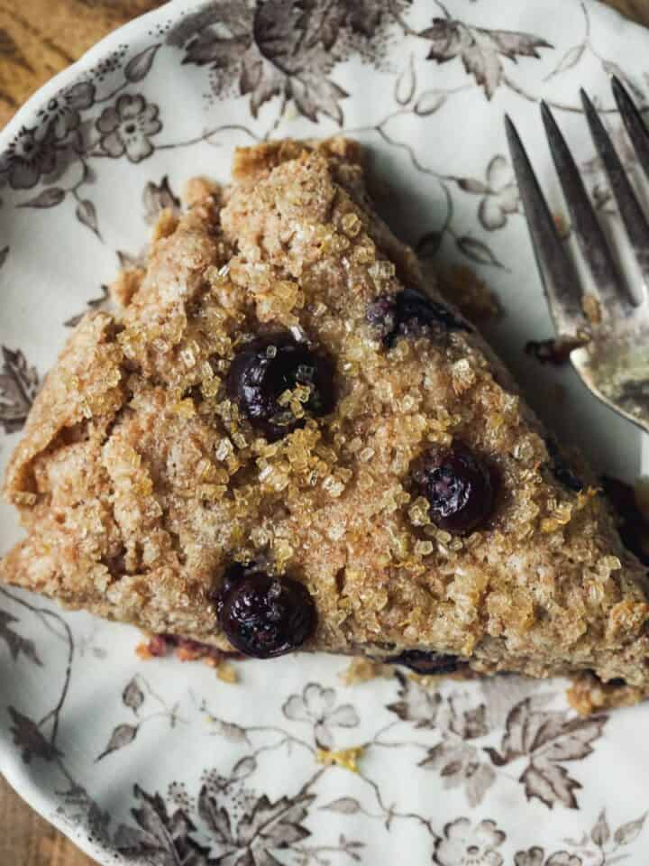 Lemon blueberry scone on a small plate topped with lemon sugar, with a fork.