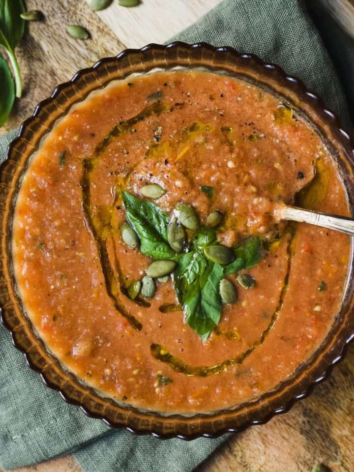 Tomato basil gazpacho in a bowl topped with fresh basil, olive oil, and pepitas.