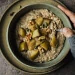 Chai oatmeal in a bowl with stewed apples, walnuts, and pepitas on top.
