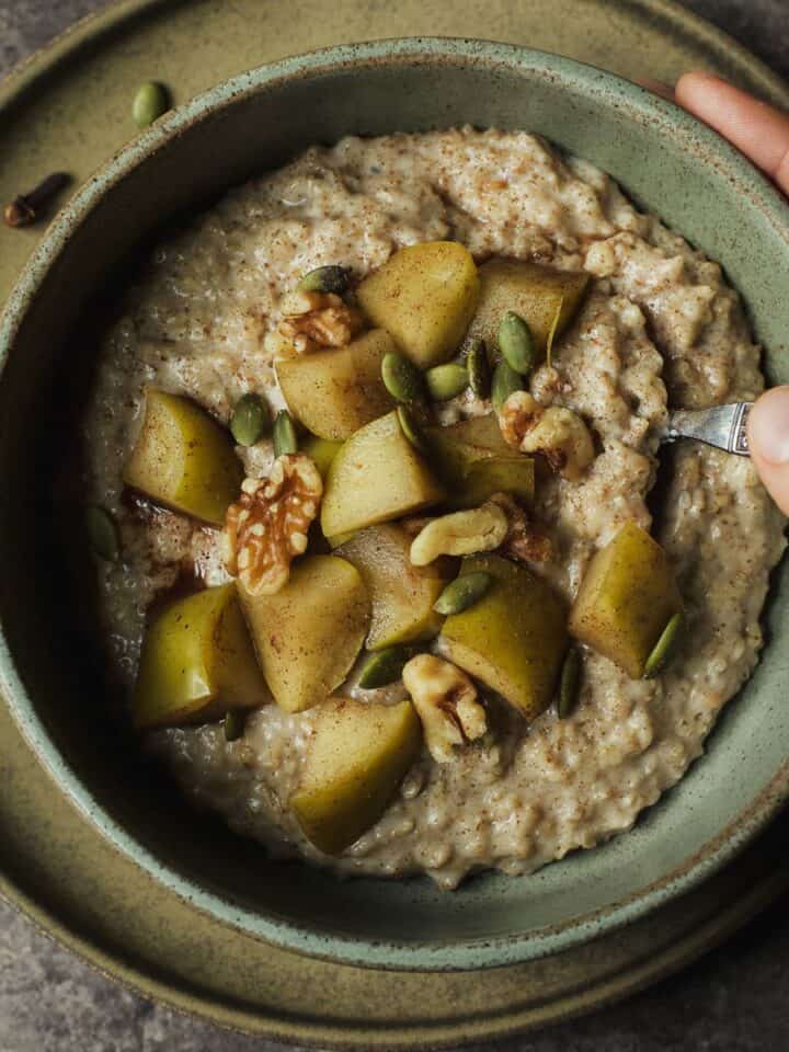 Chai oatmeal in a bowl with stewed apples, walnuts, and pepitas on top.