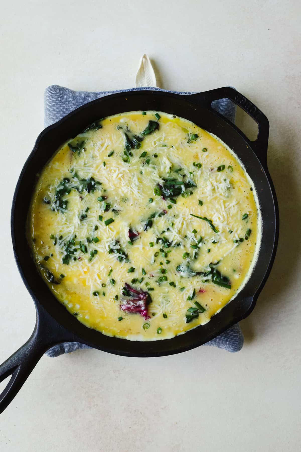 Adding whisked eggs to the cast iron skillet before baking the frittata.