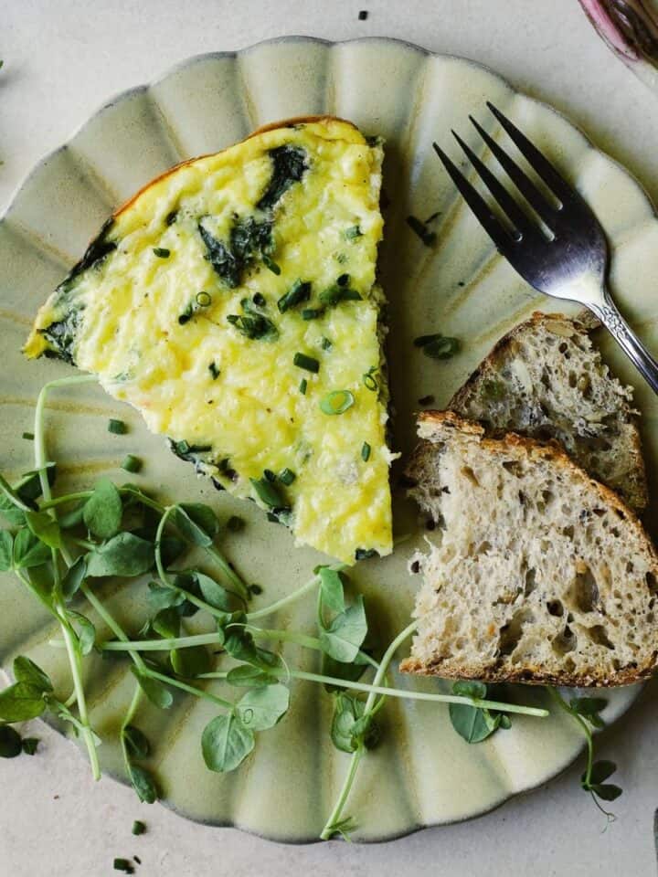 Frittata slice on a plate with toast and pea shoots.