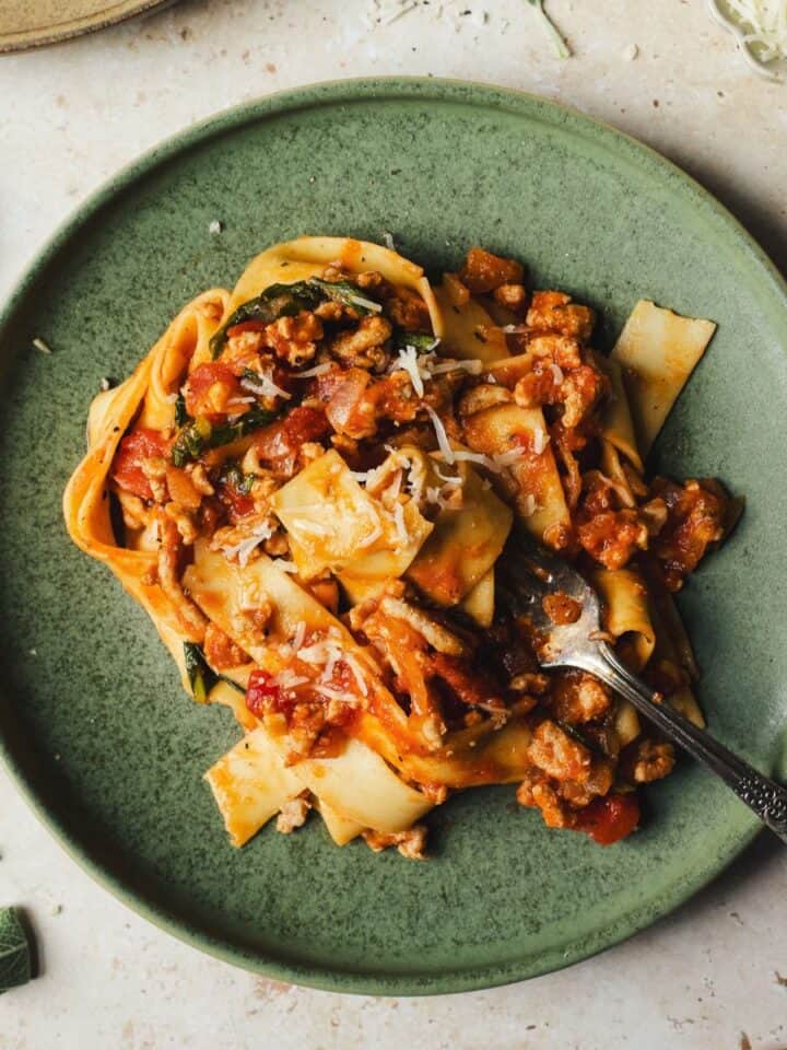 Pappardelle with meat sauce on a plate, topped with grated parmesan.